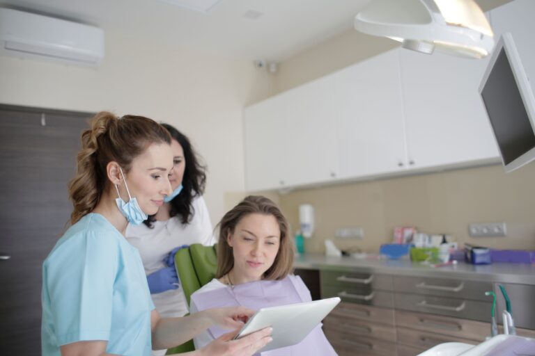 Dental professionals engage with a patient using a tablet in a clinical setting, showcasing teamwork and care.